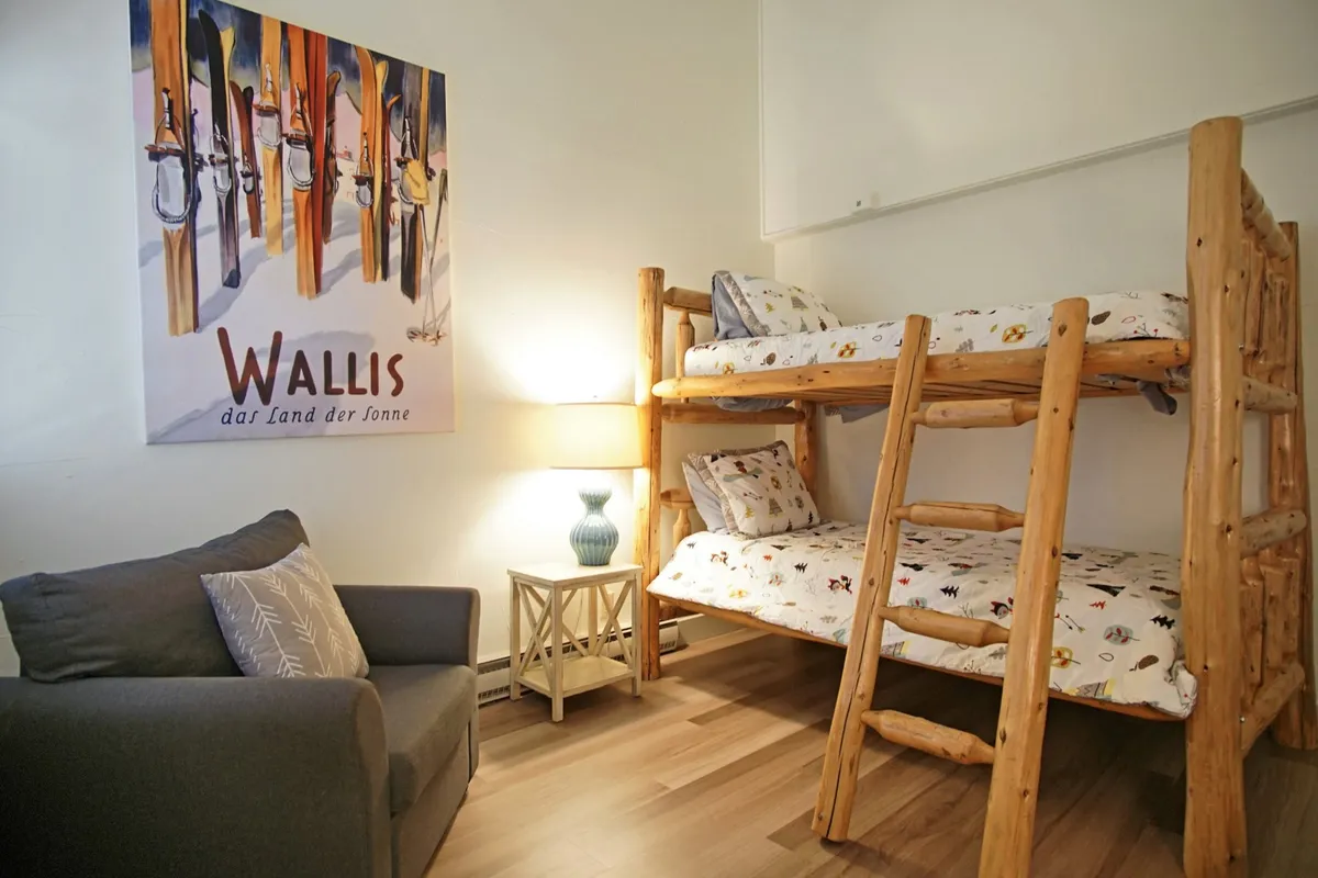A welcoming interior space with bunk beds, a sofa, wall art, and a lamp creates a homey and playful atmosphere. The setup is ideal for groups or families traveling together, highlighting a space for relaxation, storytelling, and cozy gatherings.