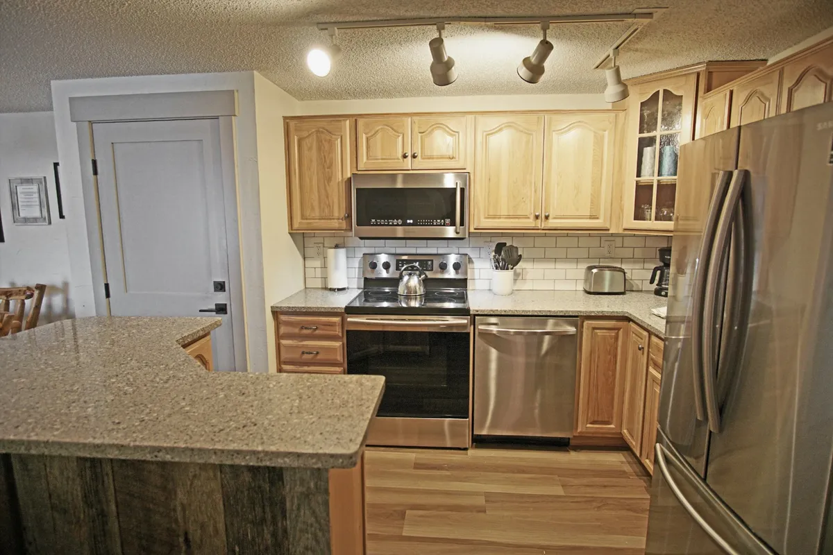 A spacious, warmly-lit kitchen with a central island, modern cabinets, and stainless steel appliances. The inviting scene suggests a hub for après-ski gatherings, home-cooked meals, and lasting memories shared by families and groups.