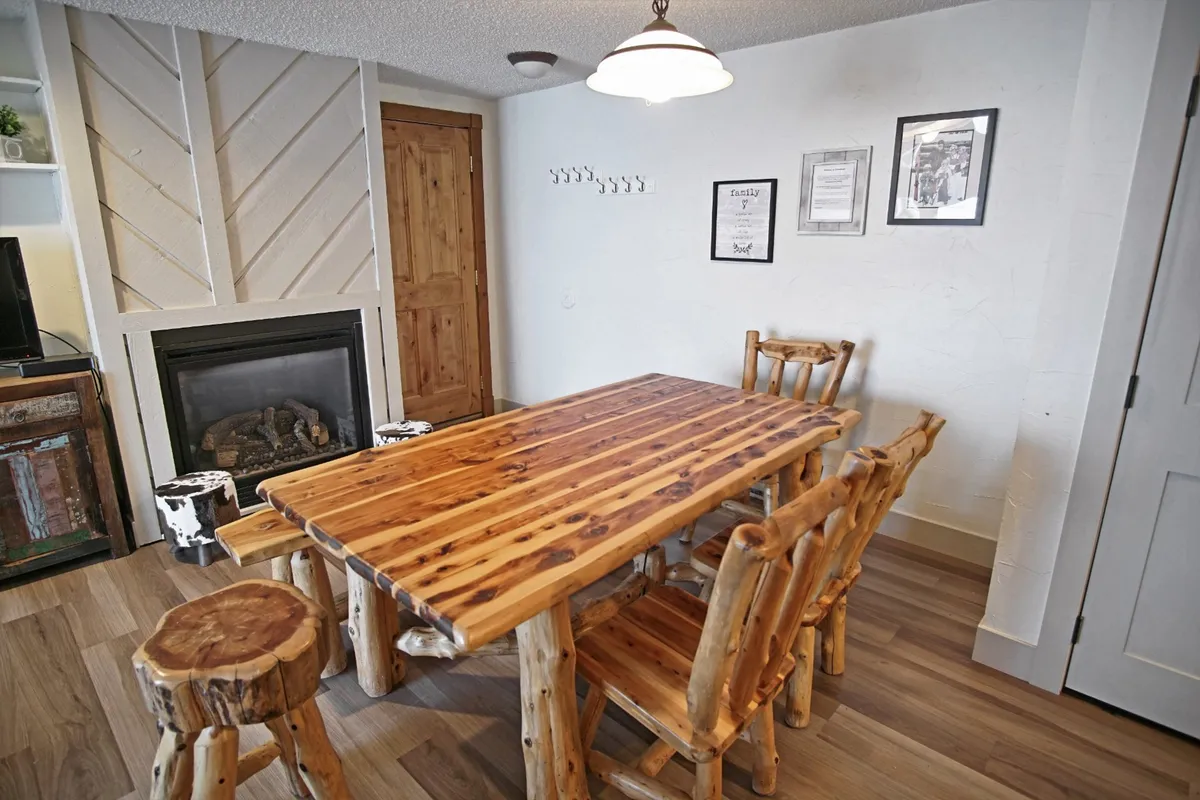 A welcoming guest lounge with a rustic wooden dining table, comfortable seating, and a glowing fireplace. The space is designed for social gatherings, family meals, and cozy group activities.