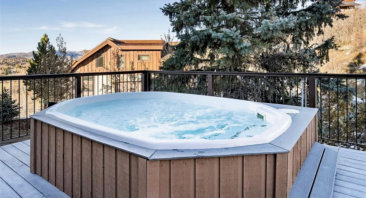 This image shows a tranquil outdoor hot tub set on a deck, surrounded by natural landscape and mountain views. The hot tub area is inviting, providing a shared space for guests to relax and socialize while soaking in the scenery.