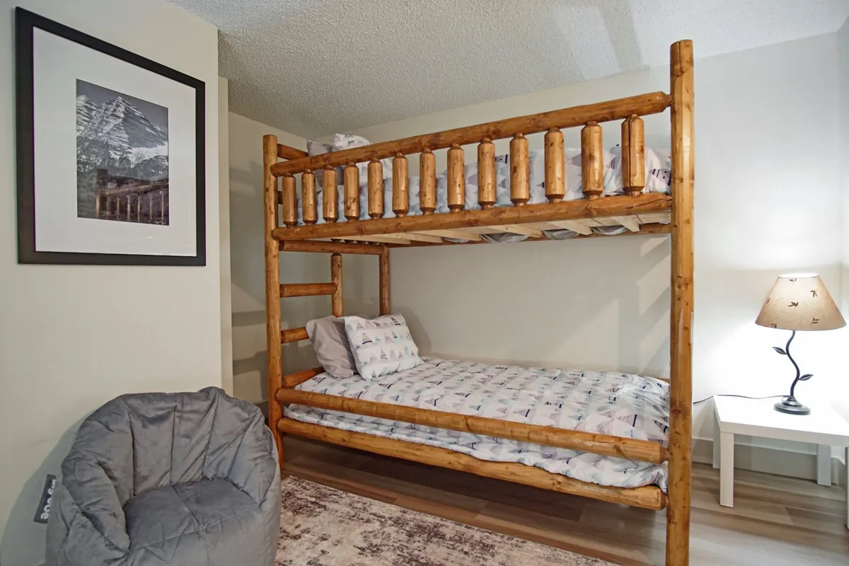 A playful, inviting bedroom with a sturdy bunk bed, a bean bag chair for reading or lounging, a table lamp for soft lighting, and colorful framed artwork. The space is designed for versatility, making it perfect for children, teens, or singles.