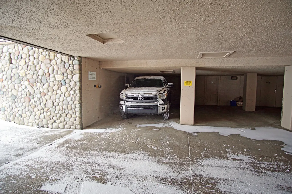 This image features a snow-covered truck parked next to a stone wall and garage structure, suggesting a protected entry and parking area beneath winter conditions. The scene highlights the practicality of covered parking and ease of access despite snowy weather.