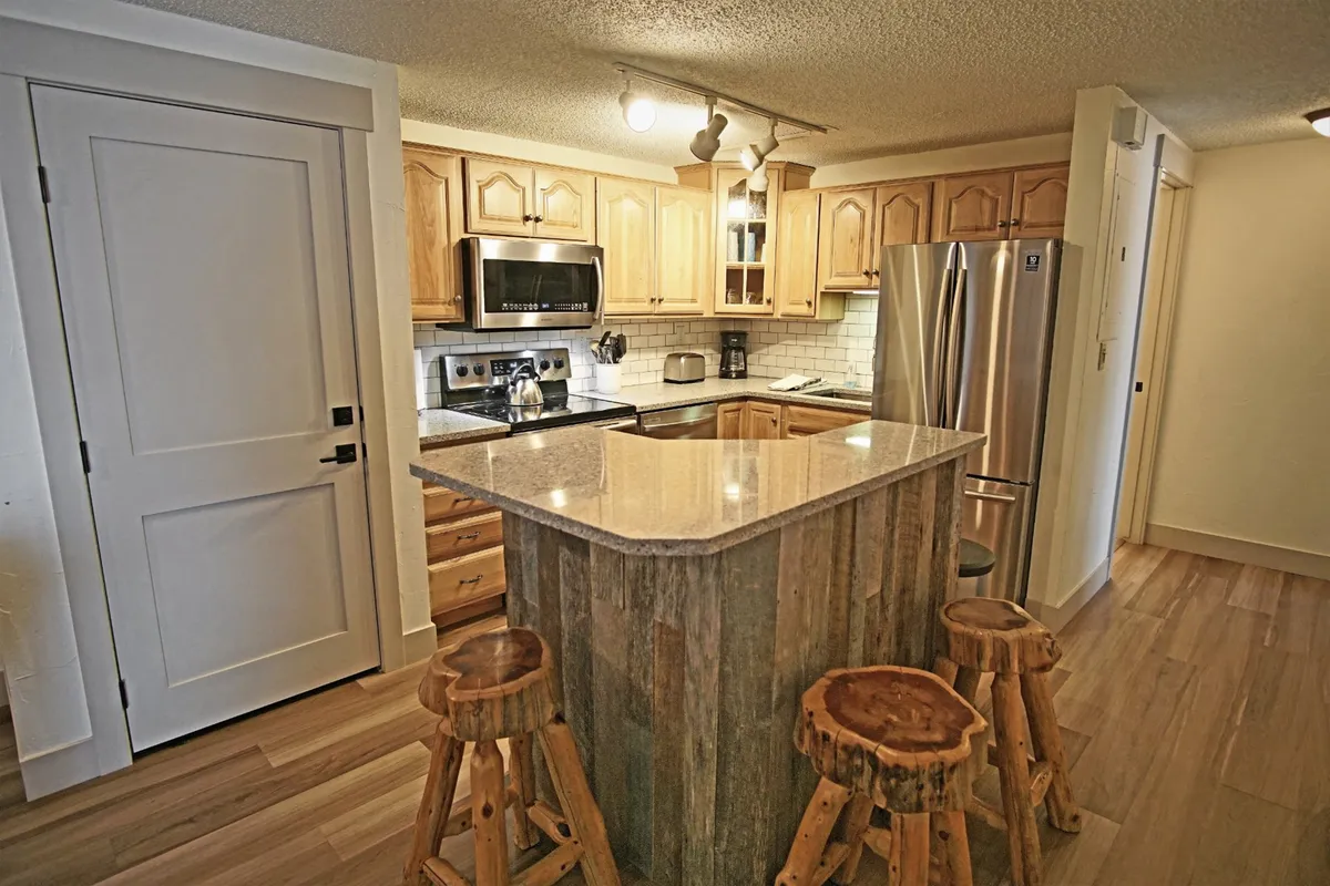 A modern kitchen and dining area with a kitchen island, stools, and appliances, offering a warm, welcoming vibe for cooking and entertaining. This space is perfect for preparing meals, gathering for snacks, or hosting casual get-togethers.
